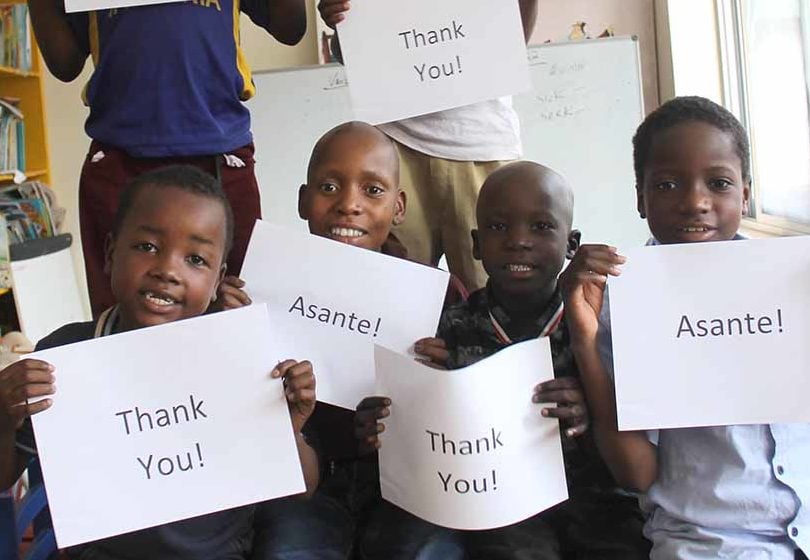 Tanzanian children hold signs that say, "Thank you!" and "Asante!"