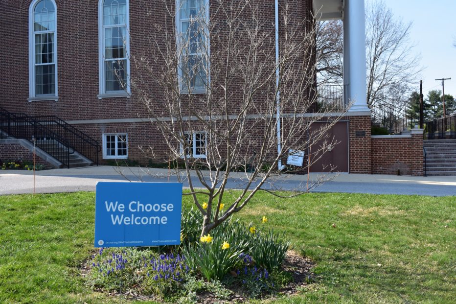 A sign reading, "We Choose Welcome" is displayed on the church grounds.