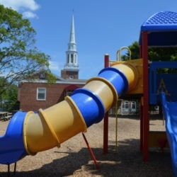 A tube slide on the church playground with the church's steeple in the background.