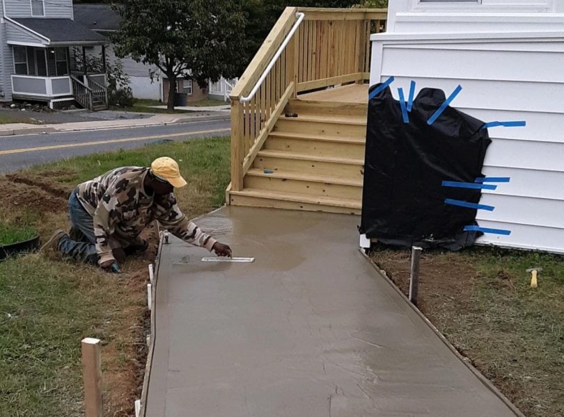 A worker smooths wet concrete on a new sidewalk.