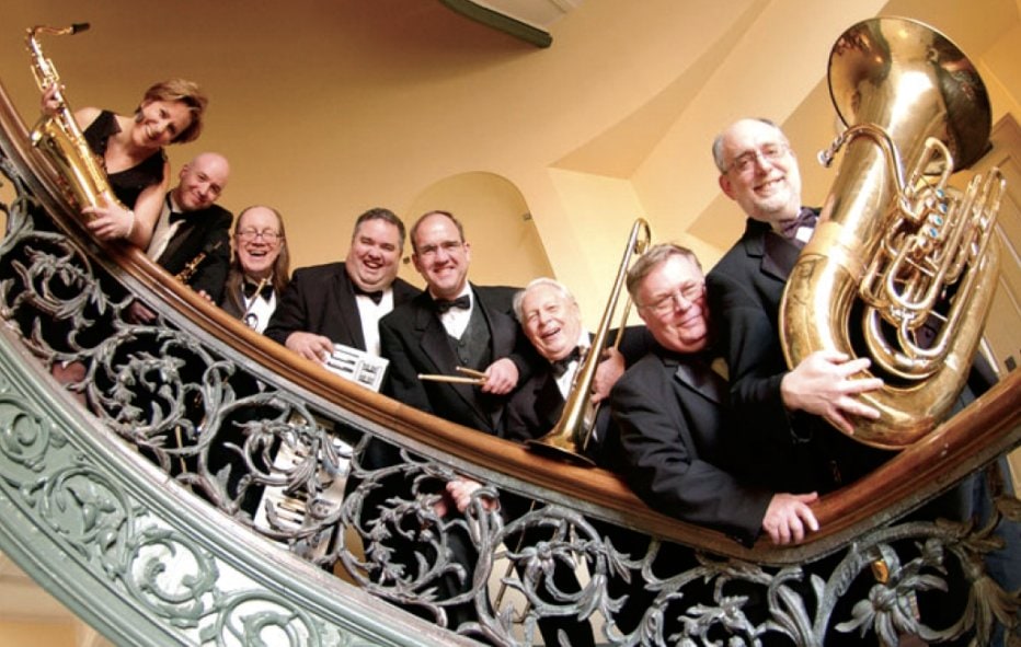 Peabody Ragtime Ensemble: 8 musicians hold their instruments and smile as they lean over a stair railing