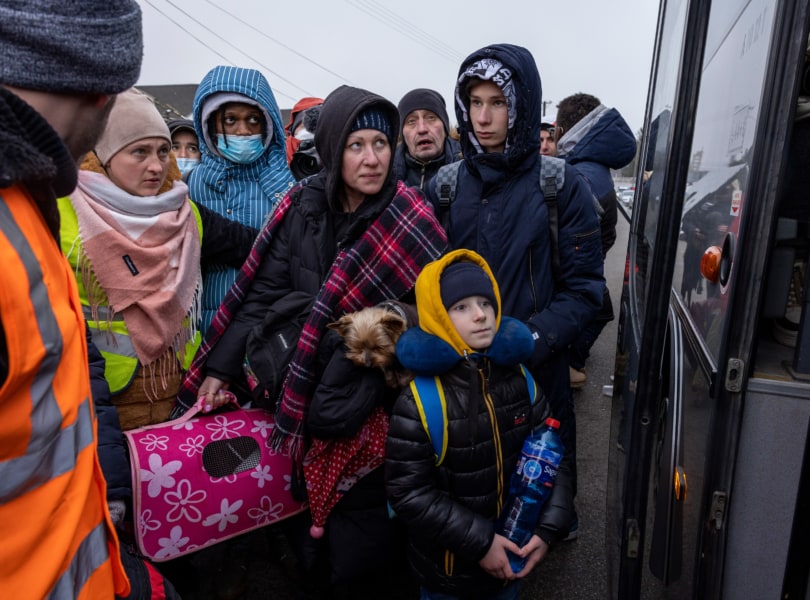 Refugees huddle in cold weather outside bus