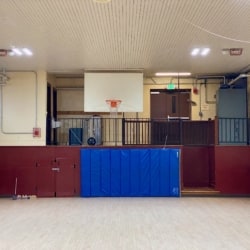 Gymnasium with hardwood floor, safety padding, and basketball hoop